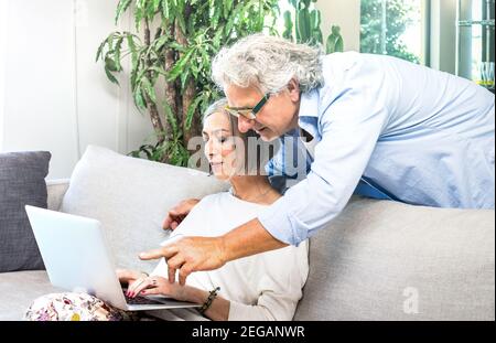 Senior retired couple using laptop computer at home on sofa - Elderly and technology concept with mature people watching shop online Stock Photo