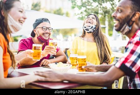 Young people drinking beer with open face masks - New normal lifestyle concept with friend having fun together talking on happy hour at brewery bar Stock Photo