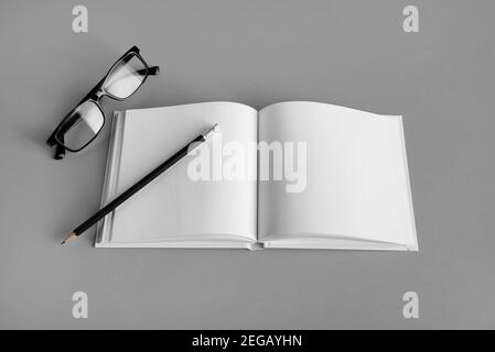 Mockup of opened blank brochure, pencil and glasses on gray paper background. Responsive design template. Stock Photo