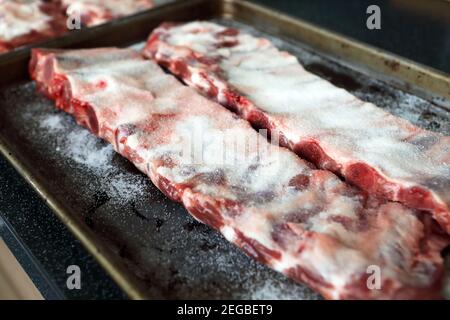 Pork spare ribs covered in salt, dry brining, which is washed off after an hour or so prior to cooking Stock Photo