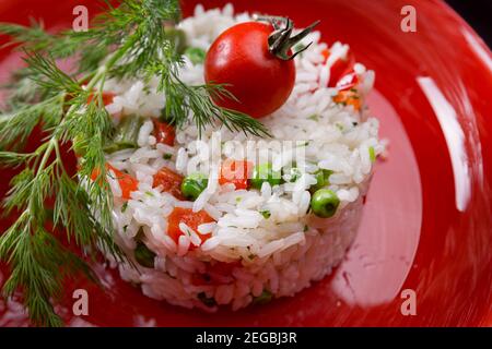 White long-grain rice with vegetables and herbs, on a red plate, close-up Stock Photo