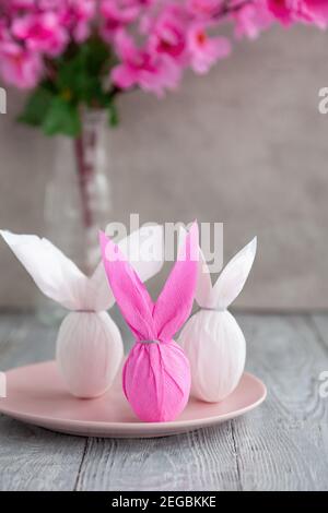 Three eggs bunny in a colored paper wrapper on a plate, nearby branch of cherry blossoms. The Easter holiday is on the table Stock Photo