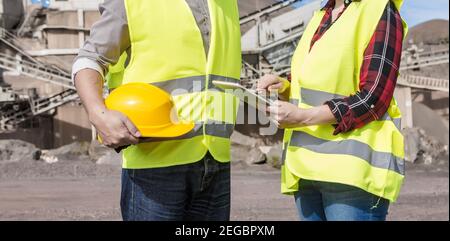 Side view of crop anonymous female engineer using tablet and checking construction plan during meeting with male colleague near industrial facility on Stock Photo