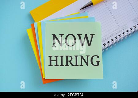 Now hiring written on colorful sticky note. light blue background. Stock Photo