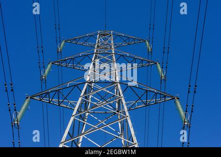 View upwards to an electricity pylon, overhead power cables and insulators set against a clear blue sky Stock Photo
