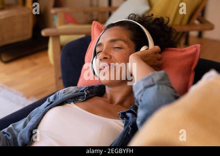 Caucasian woman lying on sofa with headphones on, relaxing at home Stock Photo