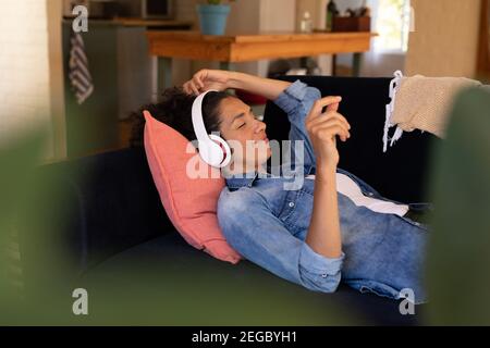 Caucasian woman lying on sofa with headphones on, relaxing at home Stock Photo