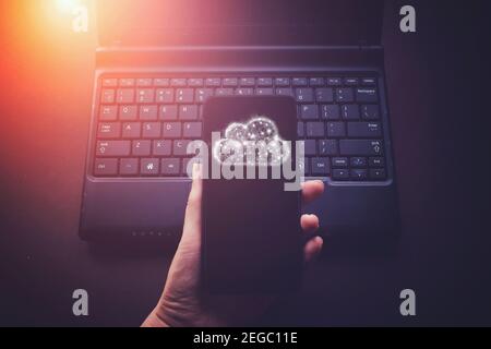 Hand hold phone with gologram cloud storage on laptop notebook keyboard background. Save information concept Stock Photo