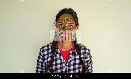 Portrait of an Indian girl with green Ayurvedic face packs isolated on white background. Women using Rose and Neem facial mask for glowing face Stock Photo