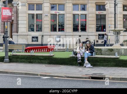 Cheltenham, Gloucestershire, UK. 18th Feb, 2021.Two girls eat lunch whilst sitting on a bench in Cheltenham, UK, during the third national lockdown. Credit: One Up Top Editorial Images/Alamy Live News Stock Photo