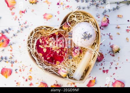 Flat lay view of various homemade spa gifts: pink soap with rose petals blossoms, bath bomb with lavender and lip balm in cardboard gift box. Stock Photo