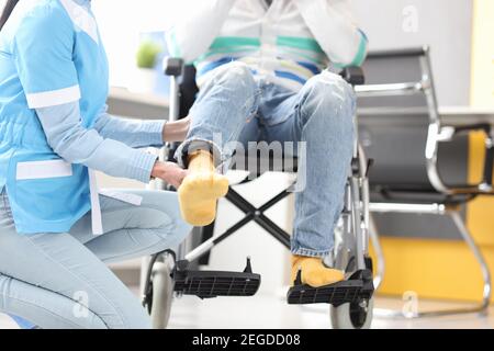 Rehabilitation doctor helping to lift leg of patient in wheelchair closeup Stock Photo