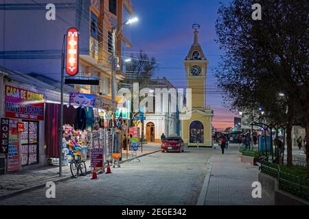 Shops in the main street and yellow clock tower in the city Uyuni after sunset, Antonio Quijarro Province, Potosí Department, Bolivia Stock Photo