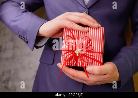 businessman man in blue suit holds gift in two hands. Red box decorated with bow. Stock Photo