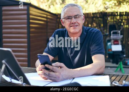 Small business owner working on laptop with workshop in background smiling at camera Stock Photo