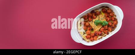 Oblong banner of the viral Feta bake pasta recipe with roasted cherry tomatoes, cheese, herbs and garlic isolated on red background with copy space Stock Photo