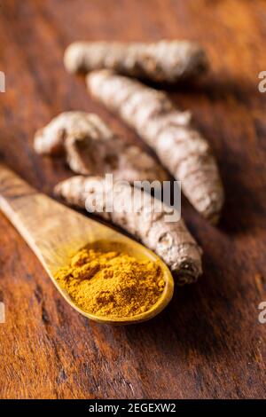 Indian turmeric powder and root. Turmeric spice. Ground turmeric in wooden spoon on wooden table. Stock Photo