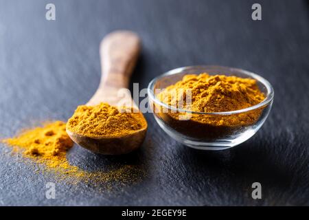 Indian turmeric powder. Turmeric spice. Ground turmeric in wooden spoon on black table. Stock Photo