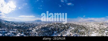 Attica Greece covered with snow, Snowy Athens panorama, sunny winter day. Aerial drone view of capital city from Penteli mount, blue sky background Stock Photo