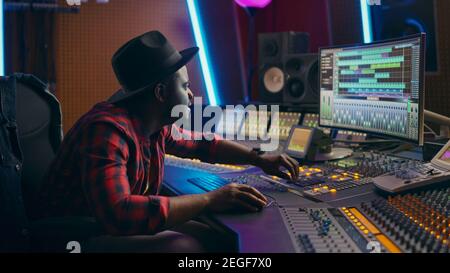 Stylish Male Audio Engineer Working in Music Recording Studio, Uses Mixing Board, Software to Create Modern Hit Song. Creative Artist Musician Working Stock Photo