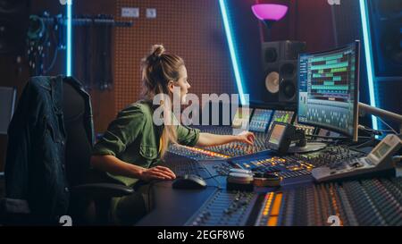 Beautiful Female Audio Engineer Working in Music Recording Studio, Uses Mixing Board and Software to Create Modern Sound. Creative Girl Artist Stock Photo