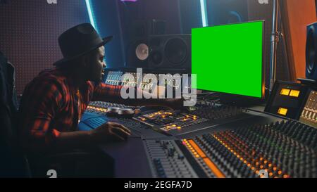 Stylish Audio Engineer Producer Working in Music Record Studio, Uses Green Screen Chroma key Computer Display, Mixer Board Equalizer and Control Desk Stock Photo