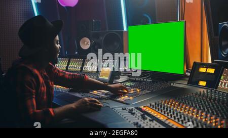 Stylish Audio Engineer Producer Working in Music Record Studio, Uses Green Screen Computer, Mixer Board Equalizer to Create New Hit Track and Song Stock Photo