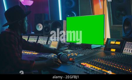 Stylish Audio Producer Working in Music Record Studio, Uses Green Screen Chroma key Computer Display, Mixer Board Equalizer and Control Desk to Create Stock Photo