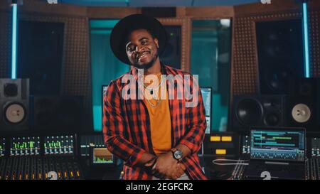 Portrait of Young Black Artist, Musician, Audio Engineer, Producer Wearing Stylish Hat and Standing in Music Record Studio. In the Background Control
