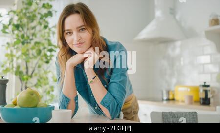 Authentic Beauty Portrait of an Attractive Brunette Female in a Bright Kitchen Room at Home. Pretty Young Woman Poses for the Camera and Gently Smiles Stock Photo