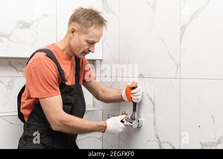 The plumber is installing a shower faucet with an adjustable wrench. Stock Photo