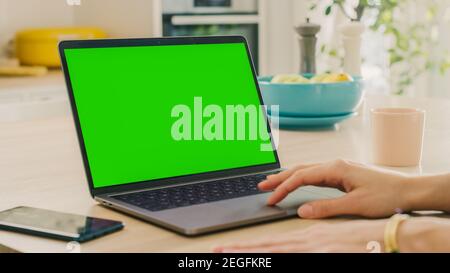 Close Up Green Screen Mock Up on a Laptop Computer. Device is Used on a Kitchen Table in a Modern Home. Person Uses Touch Pad. Sunny Modern Kitchen Stock Photo