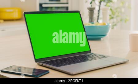 Close Up Green Screen Mock Up on a Laptop Computer. Device is Used on a Kitchen Table in a Modern Home. Sunny Modern Kitchen with Healthy Lifestyle Stock Photo