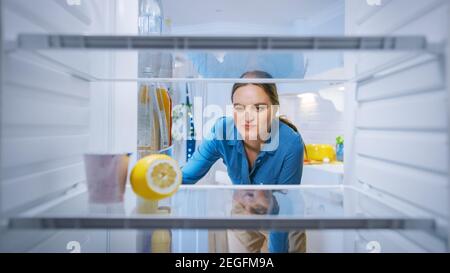 Dissappointed and Angry Young Woman Looks inside the Fridge, Checks Out that it's Empy. Point of View POV from Inside of the Kitchen Refrigerator Stock Photo