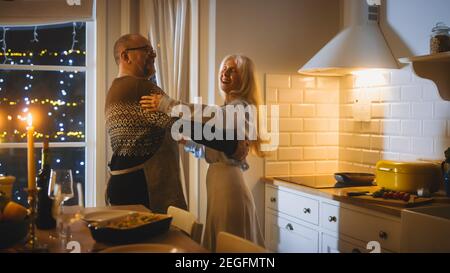 Happy Senior Couple in Love Have Romantic Evening, Dancing in the Kitchen, Celebrating Anniversary. Romantic Evening with Wine, Festive Table in Stock Photo