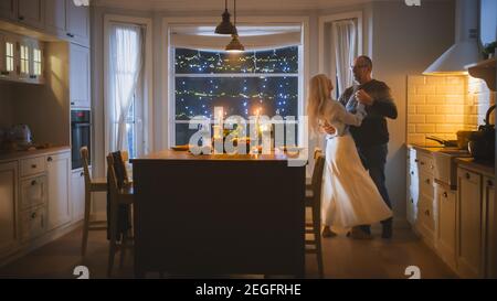 Happy Senior Couple in Love Have Romantic Evening, Dancing in Kitchen, Celebrating Anniversary. Elderly Lovely Husband, Wife Have Romantic Evening Stock Photo