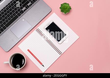 flat lay, view from the top of the office desk table. Working space notepad, laptop, phone and coffee cup on a pink background. high quality Stock Photo