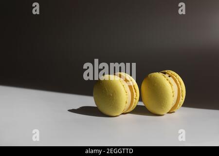Sweet yellow lemon french macaroons or macarons dessert isolated on white background with light rays from window. Stock Photo