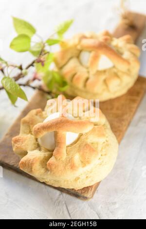 Homemade sweet Italian Easter Bread Rings with eggs called puddica in Puglia, on an old wooden cutten board with spring twig, close-up. Stock Photo