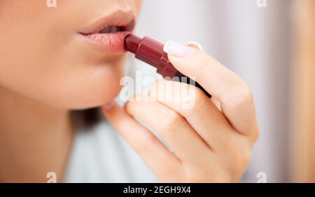 Young woman applies red lipstick to lips, makeup tutorial concept. Stock Photo