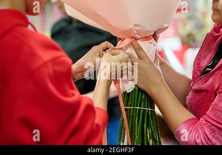 Bouquet assembly process in the workshop, two florists packing bouquet with paper and tape Stock Photo