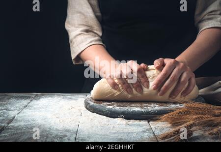 A woman kneads dough on a dark vintage background. Stock Photo