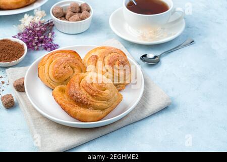 Three snail-shaped buns on a white plate against a background of a cup of tea and flowers. Stock Photo