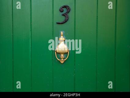 House number 3, green wooden front door with gold brass metal door knocker. Old antique painted door with knocker. UK, Suffolk Stock Photo
