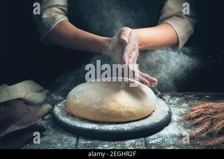 The cook's hands sprinkle the dough, and a cloud of flour flies around like dust. Stock Photo
