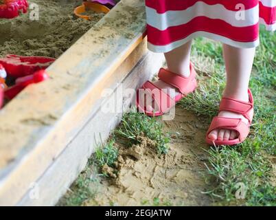 Legs of a Standing Little Girl at the Sandbox in the Summer Closeup Stock Photo