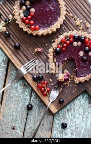 Small vegan tarts made of nuts and berry jam decorated with black, red and white currants on oak cutting board overhead view Stock Photo