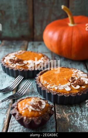 Autumn pies. Vegetarian pumpkin tartlets with nuts and oats on shabby blue background served with raw pumpkin vertical Stock Photo