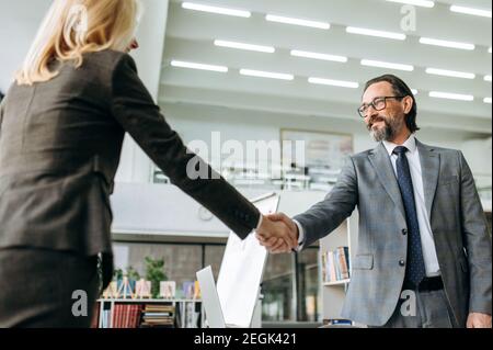 Successful business partners shaking hands on briefing meeting, starting negotiations. Influential senior coworkers coming to agreement, sign an important contract, teamwork concept Stock Photo