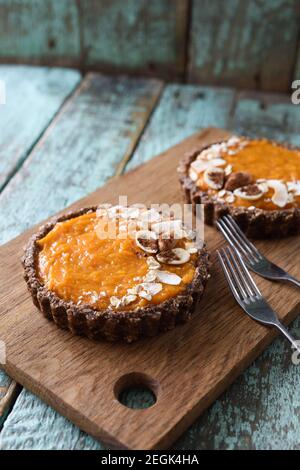 Healthy raw food dessert. Homemade open pies with almond crust and pumpkin cream filling on wooden cutting board copyspace Stock Photo